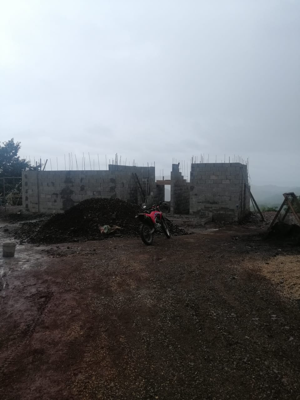 Se observa una obra en construcción con paredes de bloques de concreto y una motocicleta estacionada al frente.