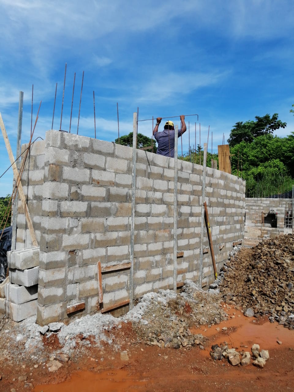 Un trabajador de la construcción coloca varillas de acero sobre una pared de bloques de concreto en una obra.