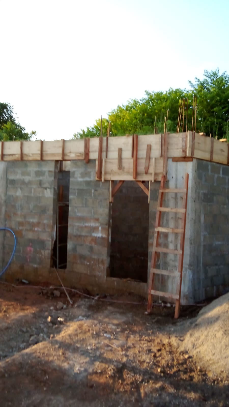 Se observa una estructura de bloques de concreto en construcción con encofrados de madera y una escalera apoyada.