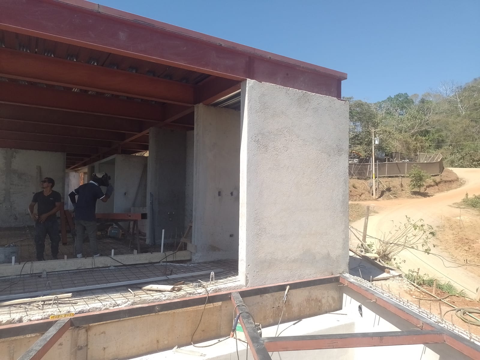 Dos trabajadores realizan labores de construcción en una estructura de concreto y vigas de acero.