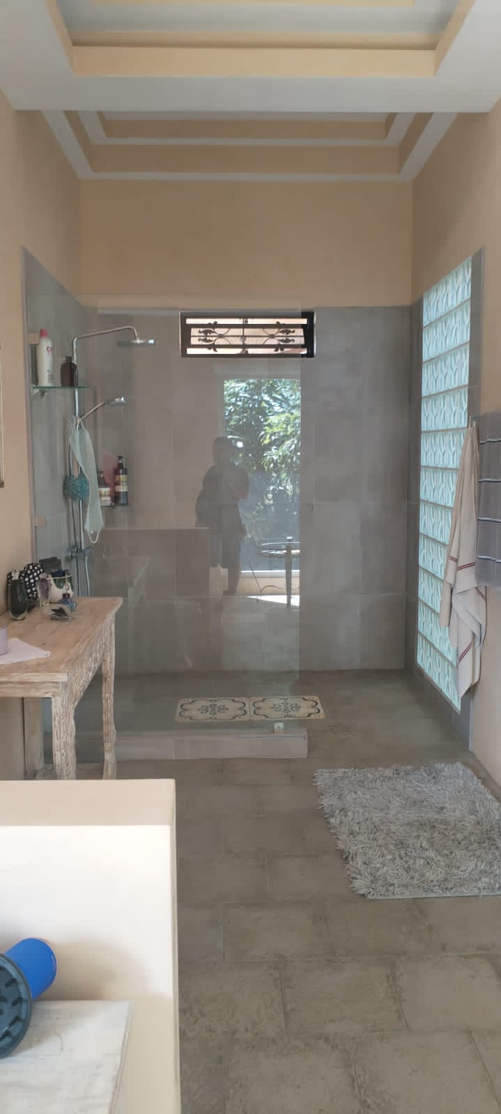 Un baño moderno con ducha de cristal, paredes de azulejos grises y una pared de bloques de vidrio.