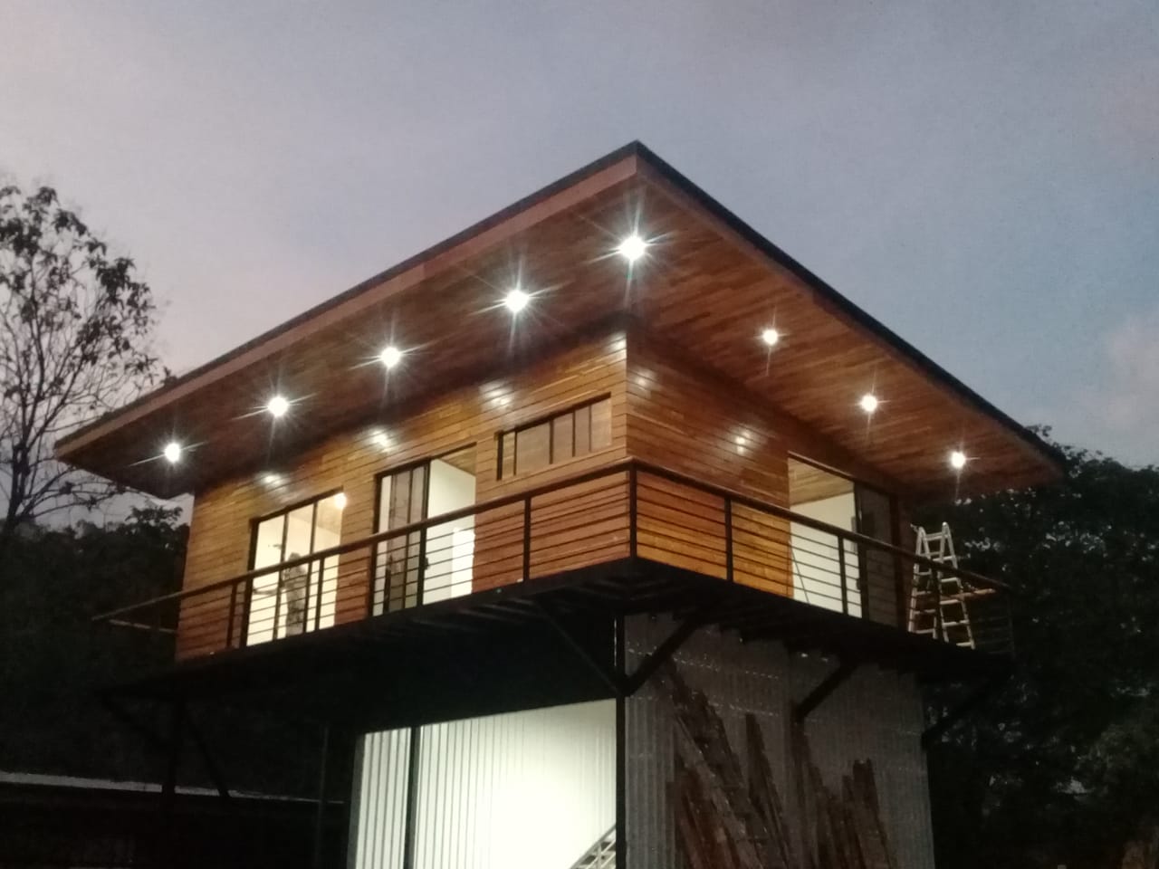 Se observa una estructura de dos niveles con acabados en madera y balcones iluminados durante el atardecer.