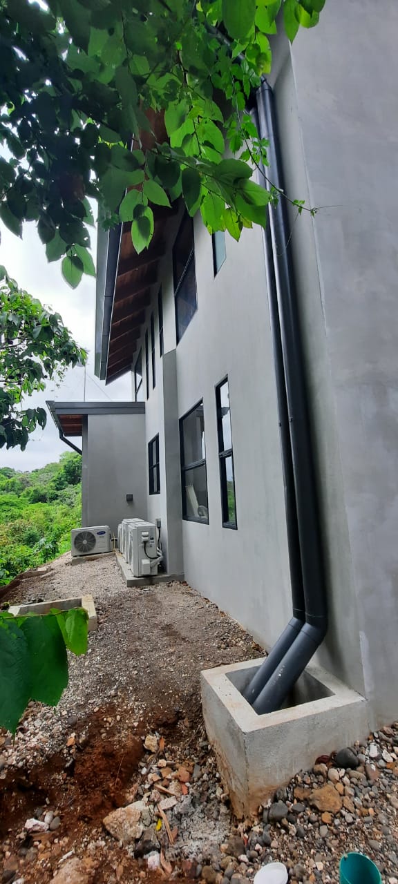 Vista lateral de una edificación moderna con paredes grises, ventanas negras y unidades de aire acondicionado exteriores.