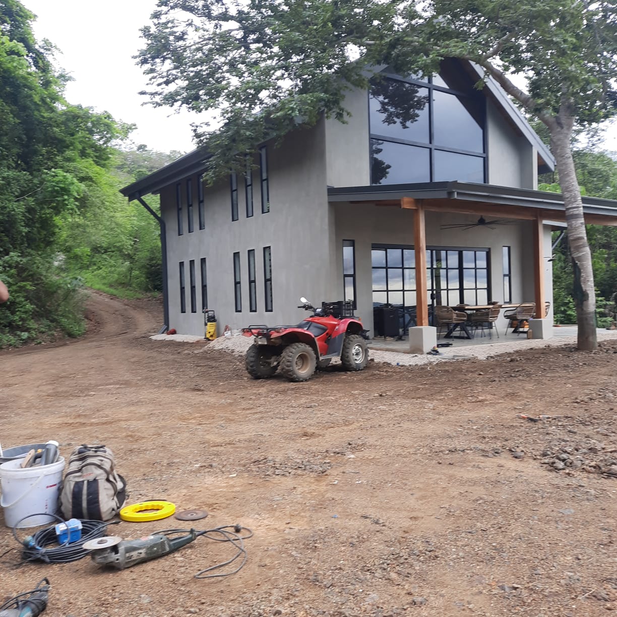 Una casa moderna de dos pisos con grandes ventanales y una cuatrimoto estacionada al frente en un terreno en construcción.