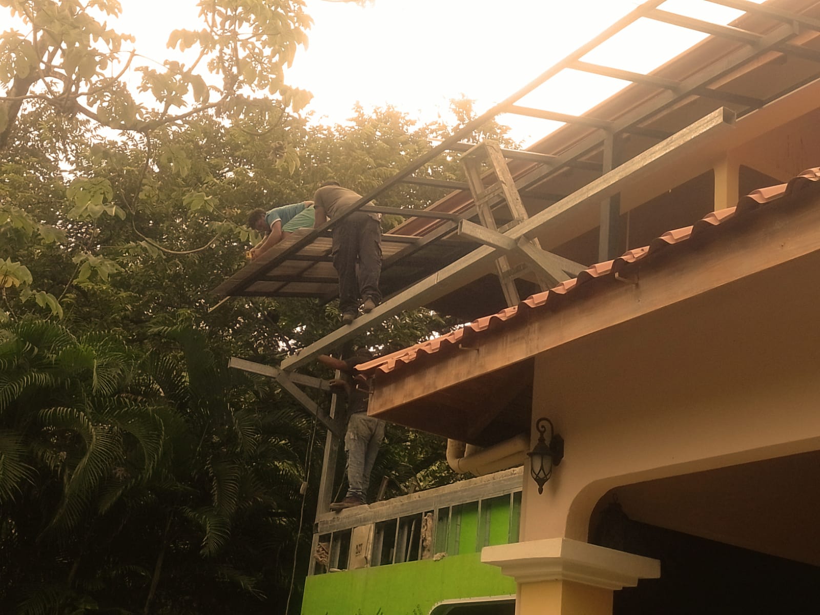 Trabajadores instalando una estructura metálica para un techo en la parte exterior de una casa.