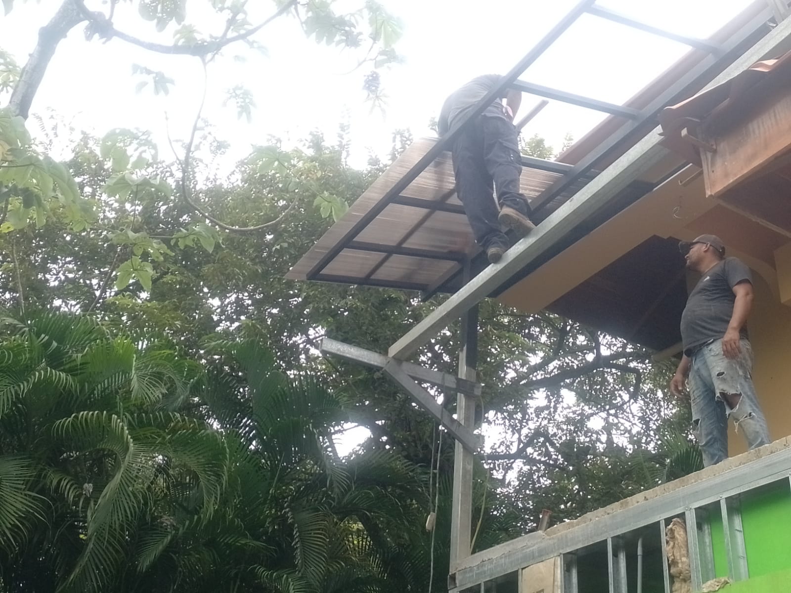 Dos trabajadores realizan la instalación de una estructura metálica y techo en una construcción exterior.