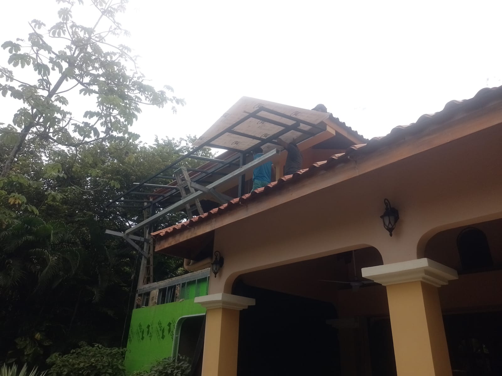 Dos trabajadores instalan una estructura metálica y paneles en el techo de una casa.