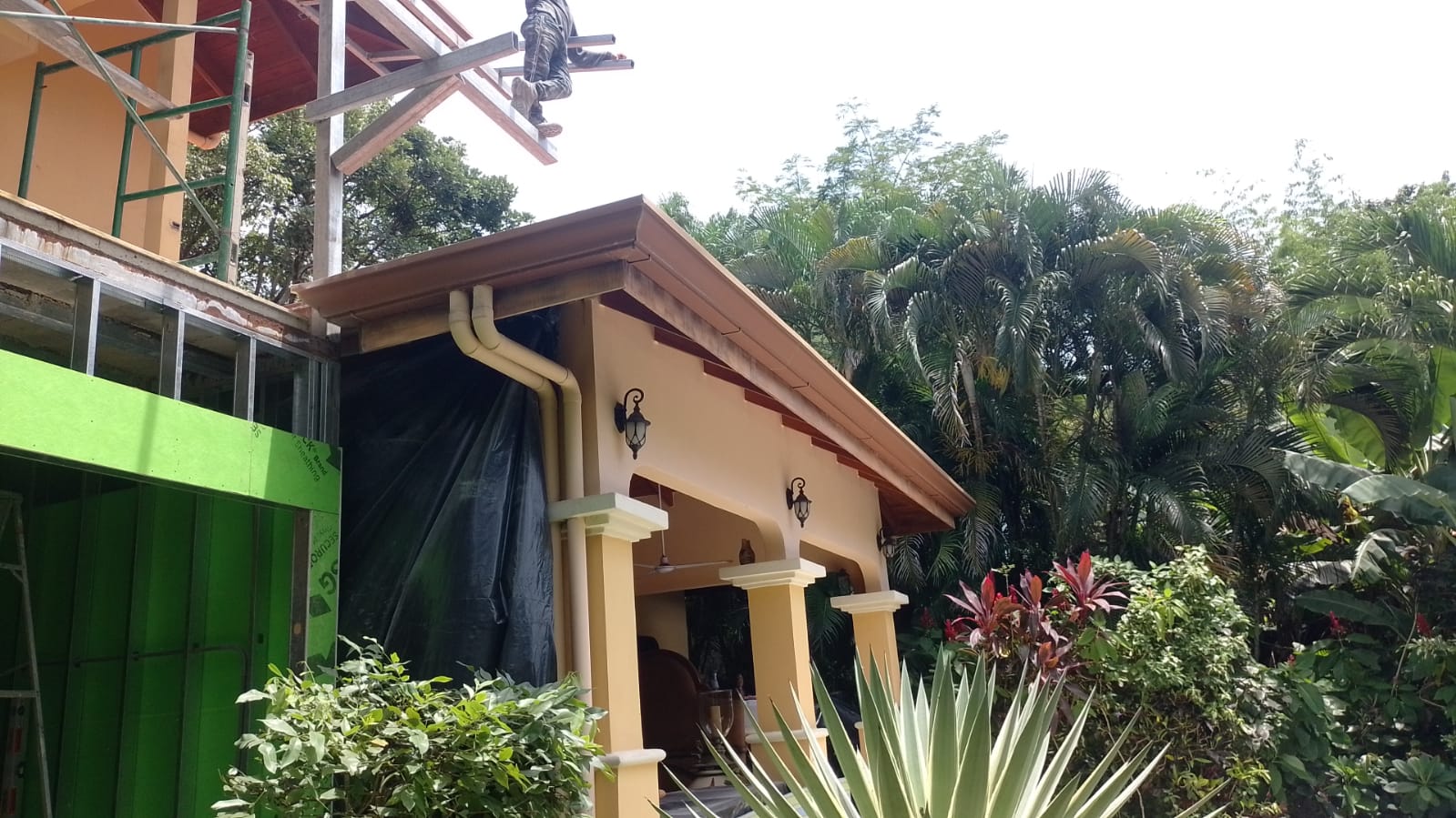 Un trabajador realiza labores de construcción y mantenimiento en el techo de una casa con estructura de metal.