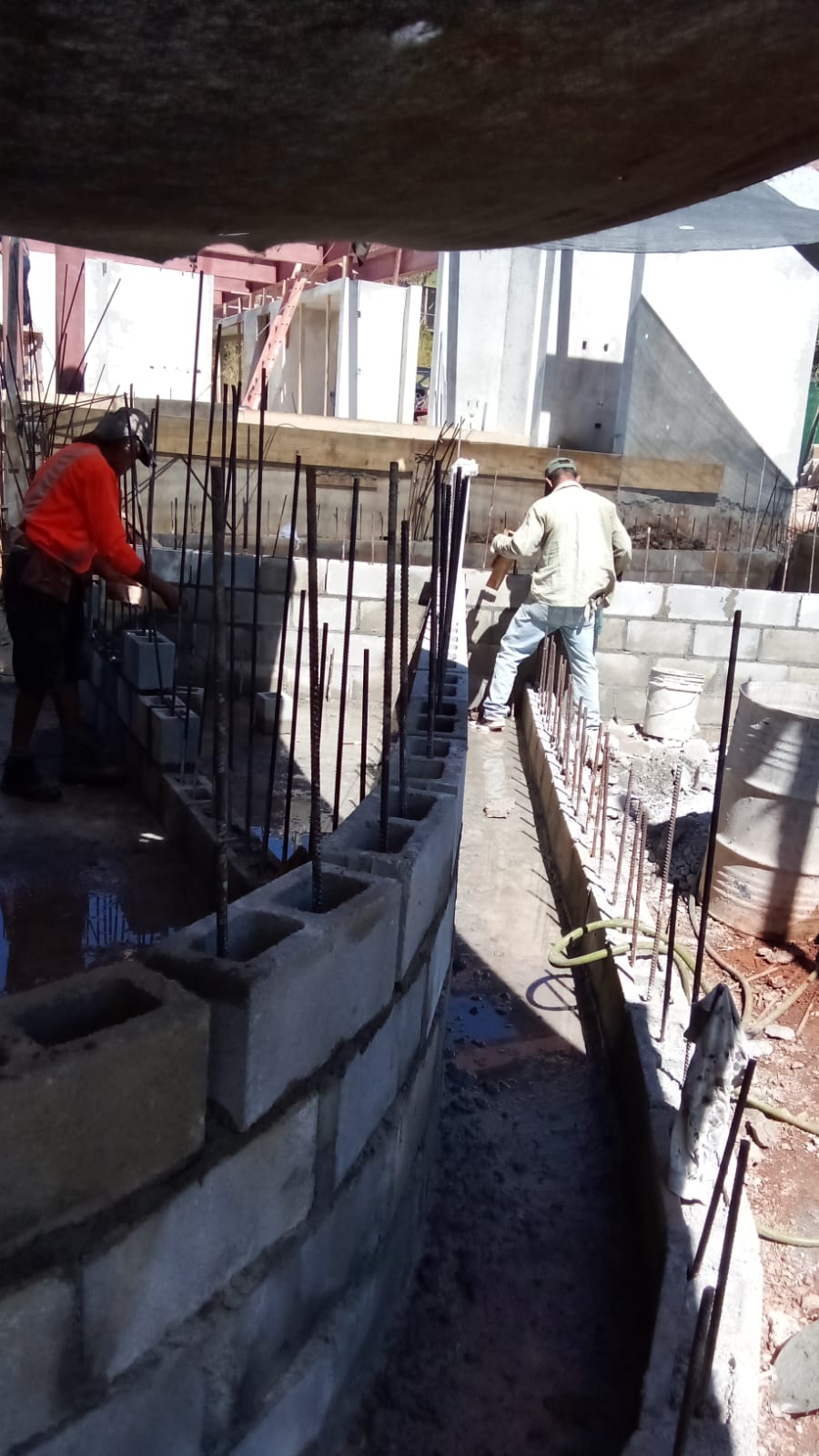 Dos trabajadores de construcción levantan una pared curva de bloques de concreto con varillas de refuerzo.