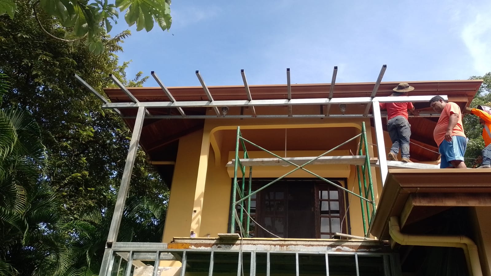 Trabajadores realizando la instalación de una estructura metálica en el techo de una casa amarilla.