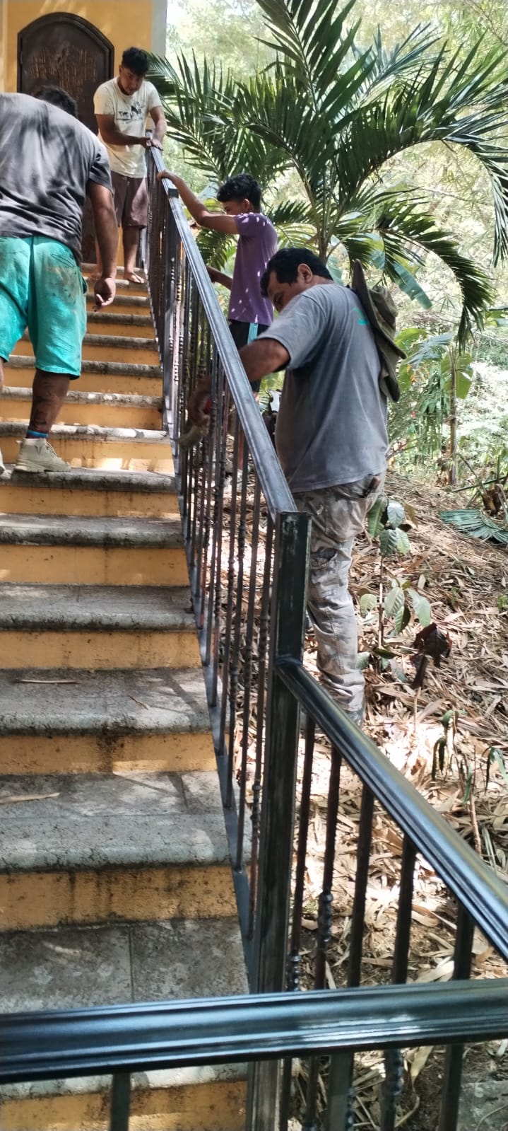 Un grupo de trabajadores está pintando el barandal de metal de una escalera exterior.