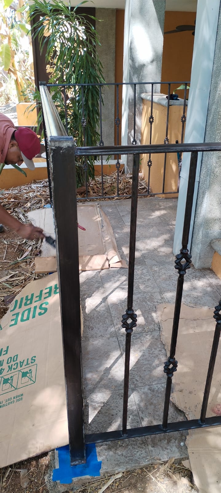 Un trabajador está pintando una barandilla de metal negro en el exterior de una casa.