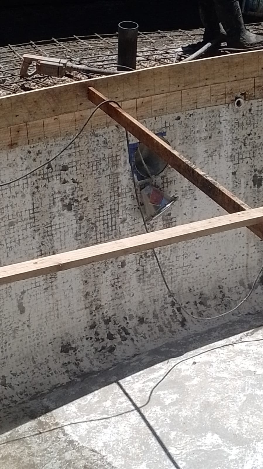 Se observa la construcción de una piscina con encofrado de madera y una lámpara instalada en la pared.