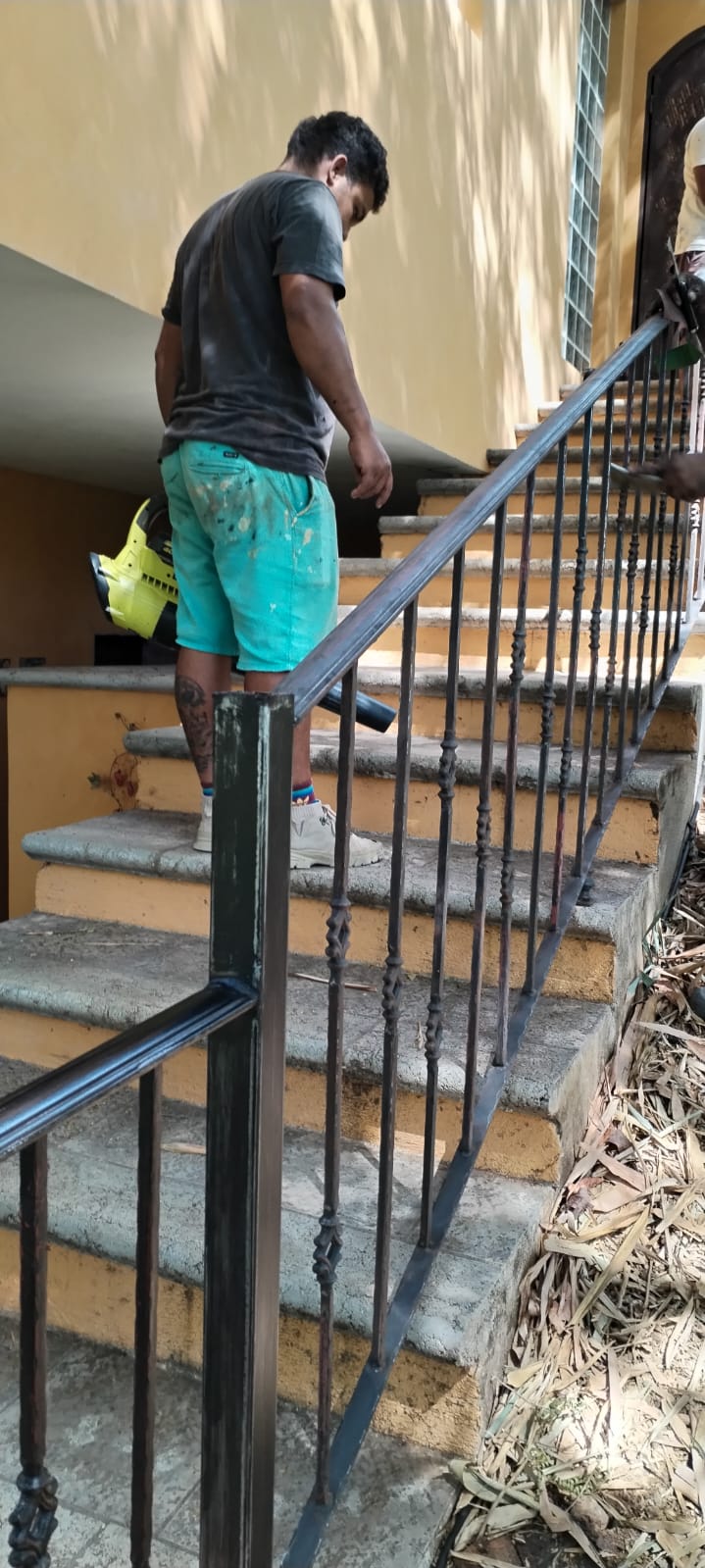 Un trabajador utiliza una sopladora de hojas para limpiar unas escaleras exteriores con barandal de metal.