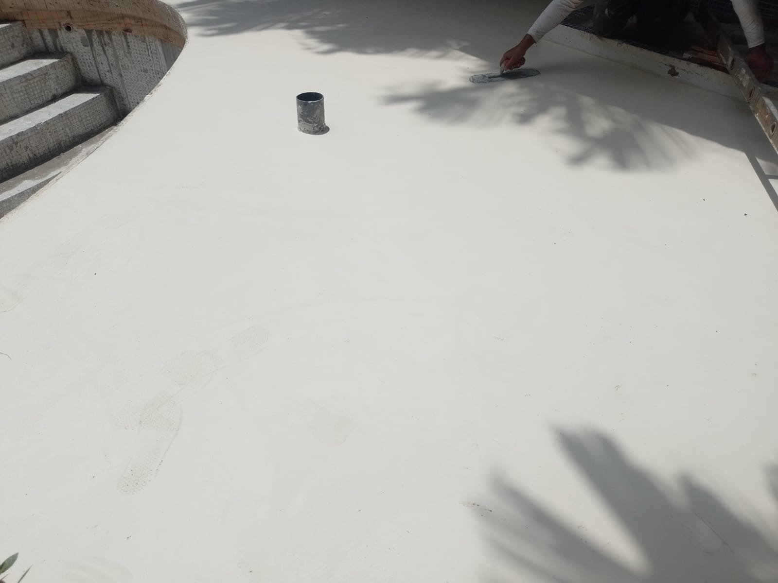 Un trabajador está aplicando una capa de acabado liso sobre una superficie de concreto cerca de una piscina.