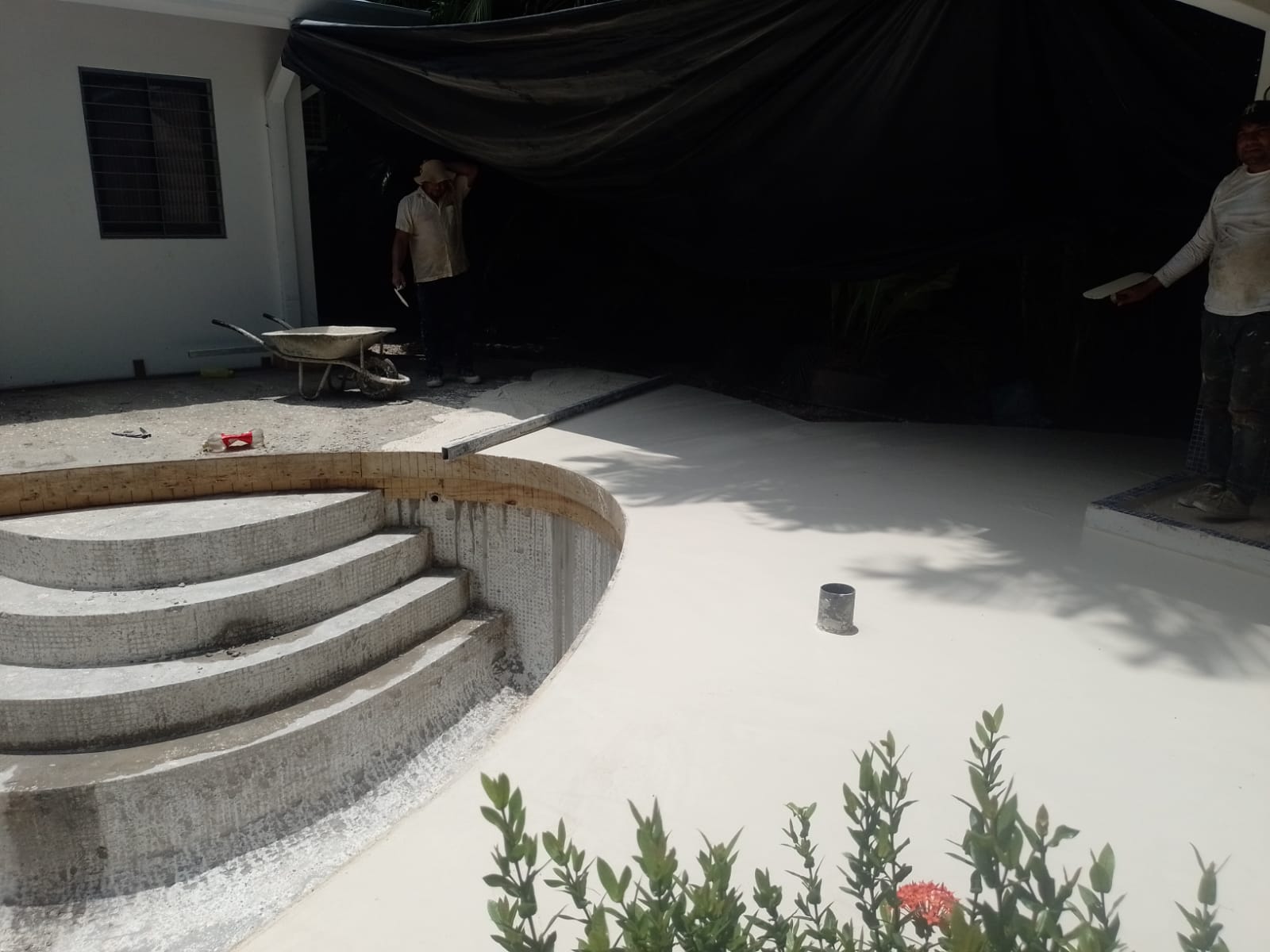 Dos trabajadores realizan labores de construcción y acabado en el área de una piscina en remodelación.