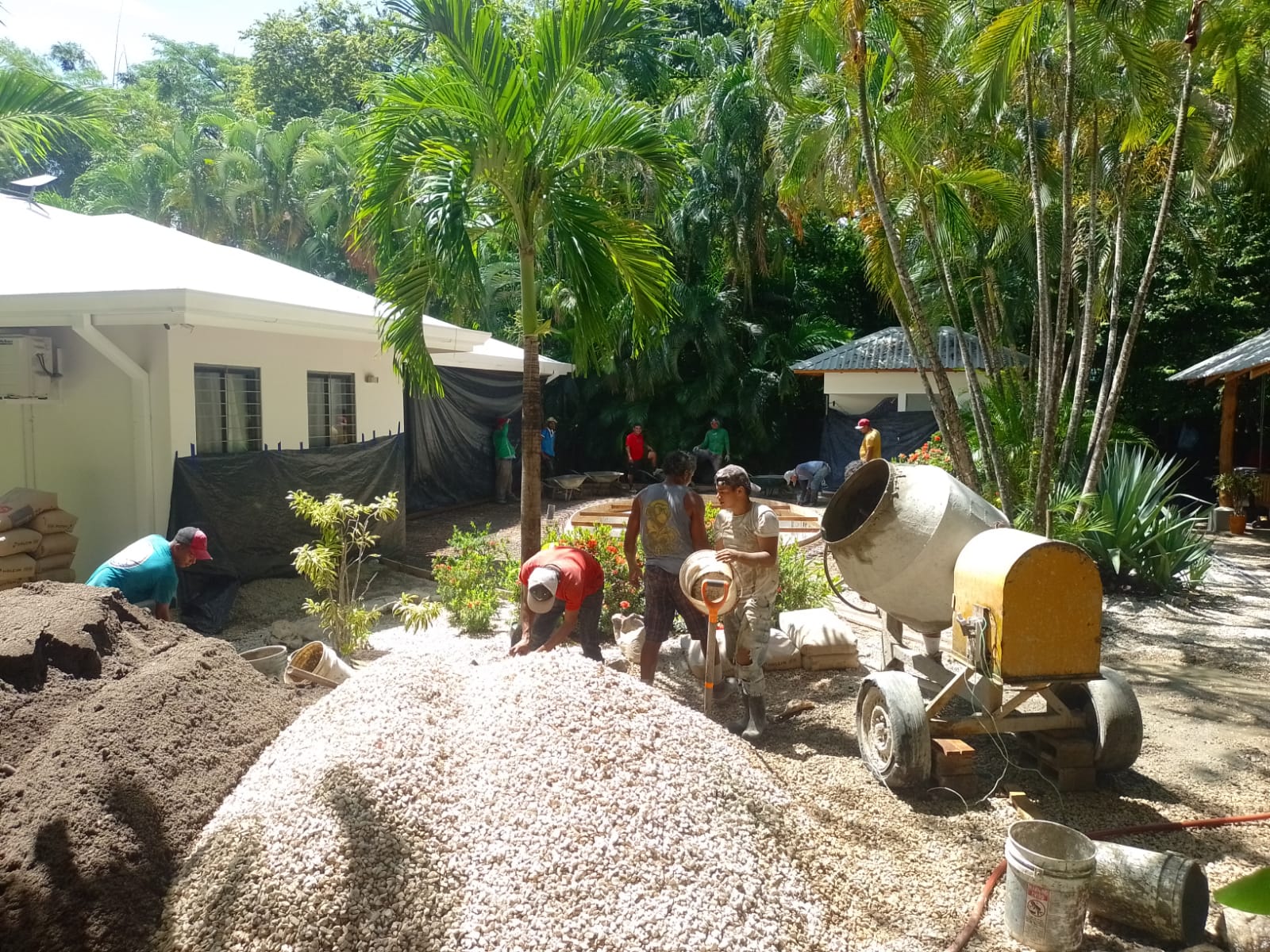 Un grupo de trabajadores realiza labores de construcción en un jardín con una mezcladora de cemento y materiales de obra.