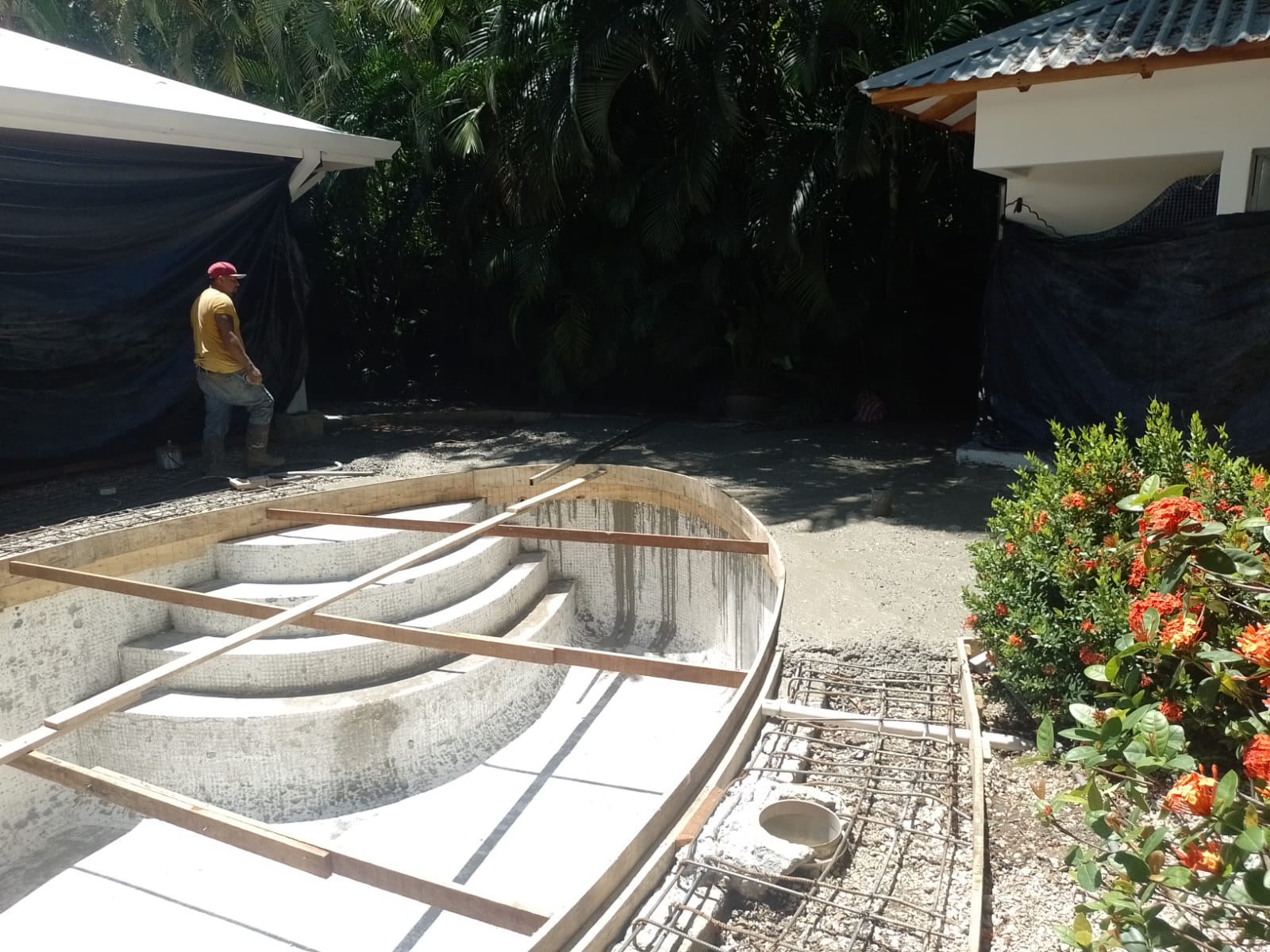 Un trabajador supervisa la construcción de una piscina con escalones curvos en un área exterior.