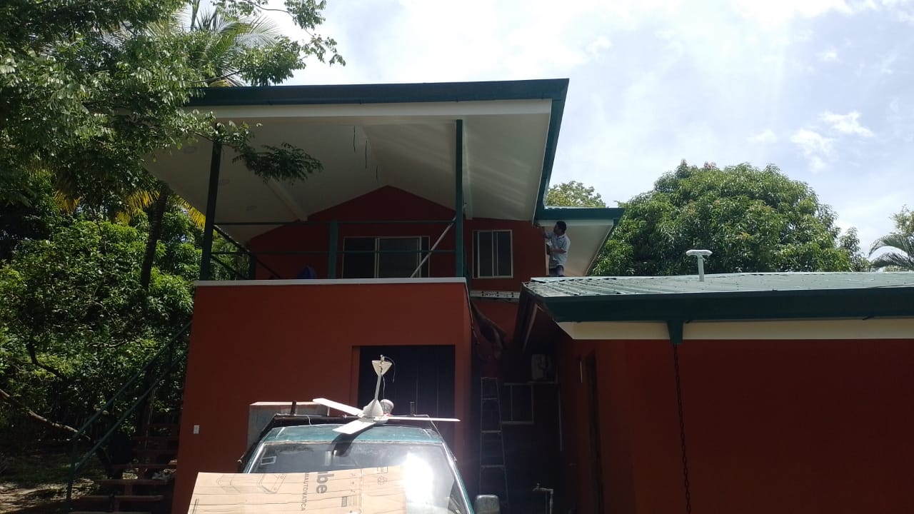 Se observa una casa de color terracota con un trabajador realizando labores de mantenimiento en la parte superior.