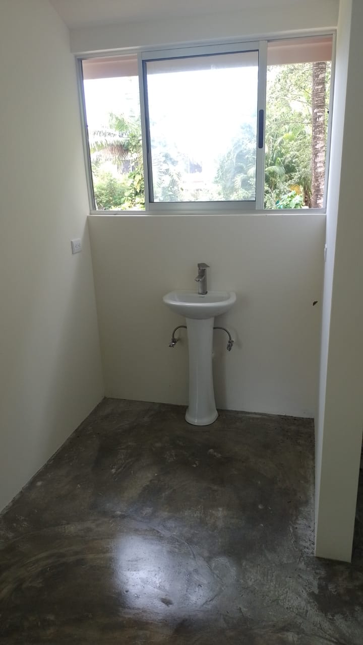 Se observa un lavamanos de pedestal blanco instalado en una habitación con paredes claras y piso de concreto pulido.