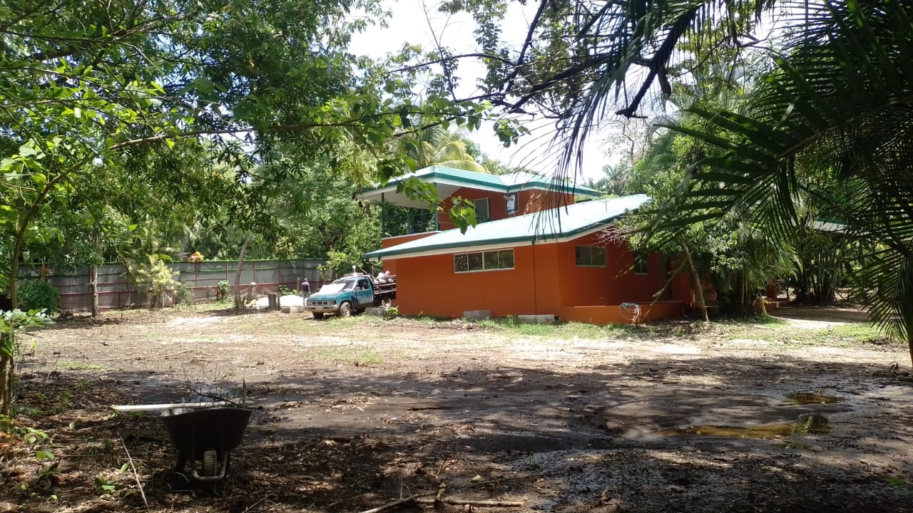 Se observa una casa de dos niveles pintada de color naranja con techo verde rodeada de vegetación.