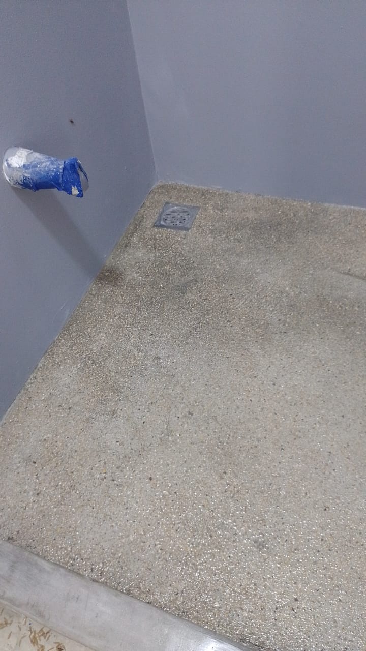 Se muestra el acabado de un piso de concreto pulido o terrazo en una esquina con un drenaje instalado.