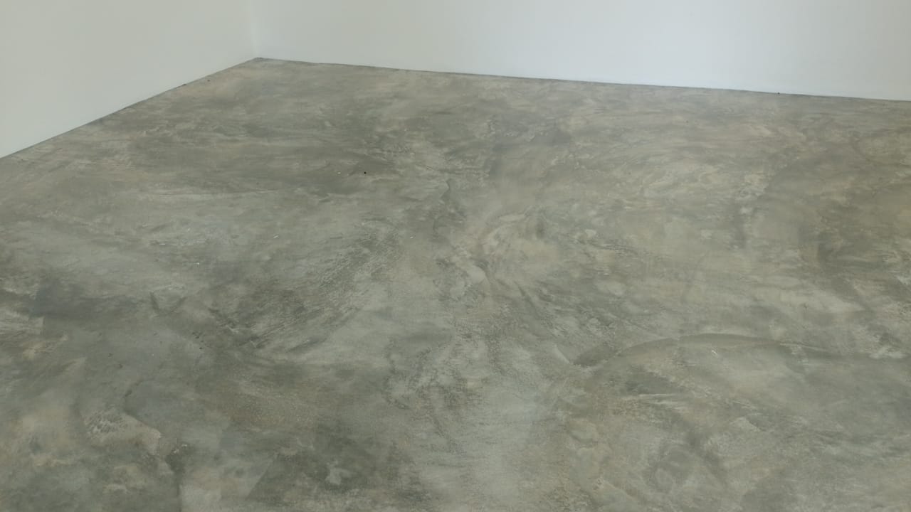 Se observa un piso de concreto pulido con acabado gris veteado en una habitación con paredes blancas.