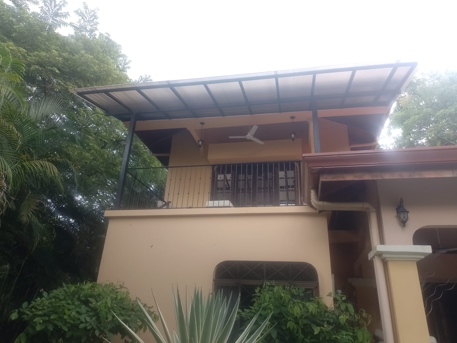 Vista exterior de una edificación de dos niveles con paredes color crema y un balcón techado.