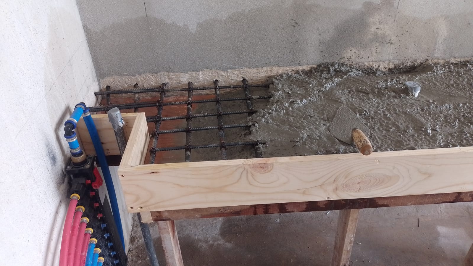 Se observa un proceso de construcción donde se está vertiendo concreto sobre una estructura de varillas de hierro y encofrado de madera.