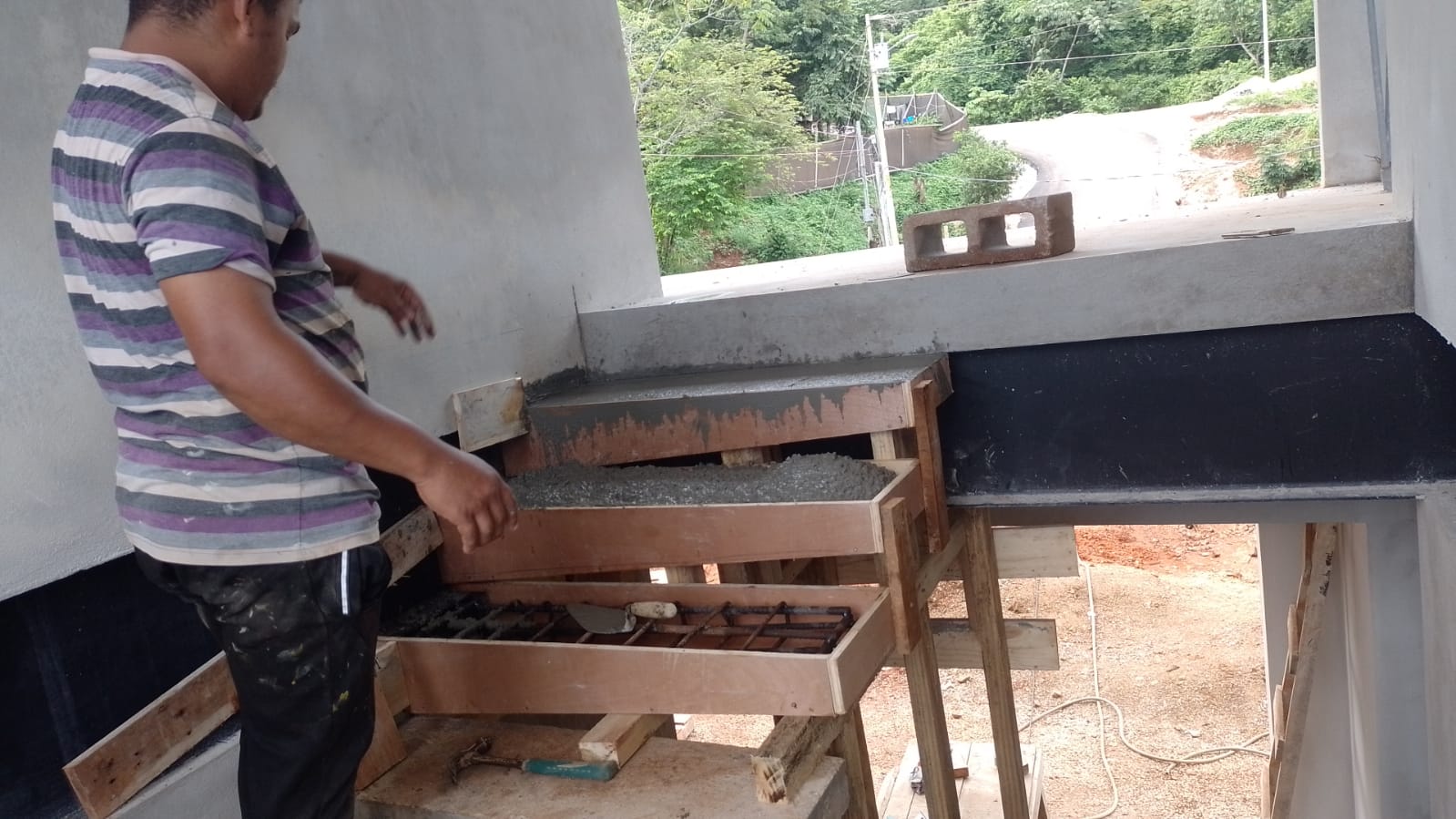 Un trabajador de la construcción está instalando encofrados de madera para verter escalones de concreto en una obra.