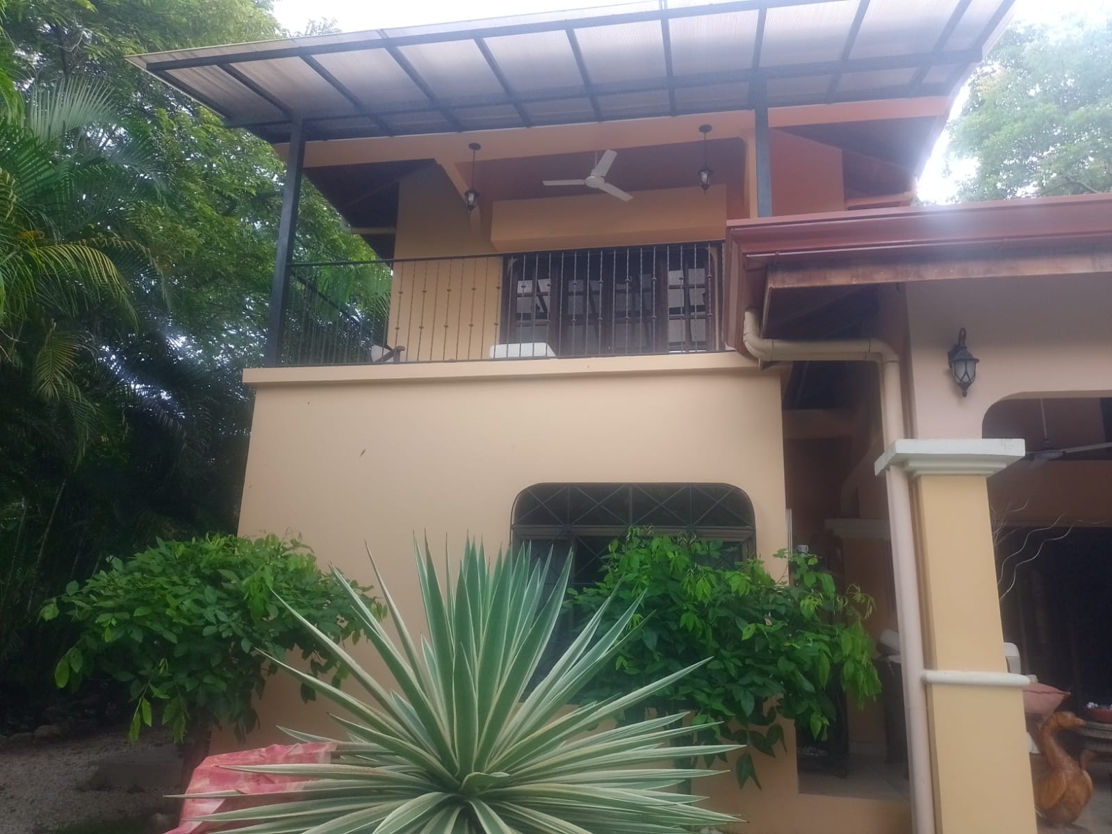 Se observa la fachada exterior de una edificación de dos niveles con paredes color crema y un balcón techado.